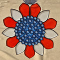A circular decorative ornament or medallion with a red and white petal-like border surrounding a blue star-patterned center, shown against a light beige background.