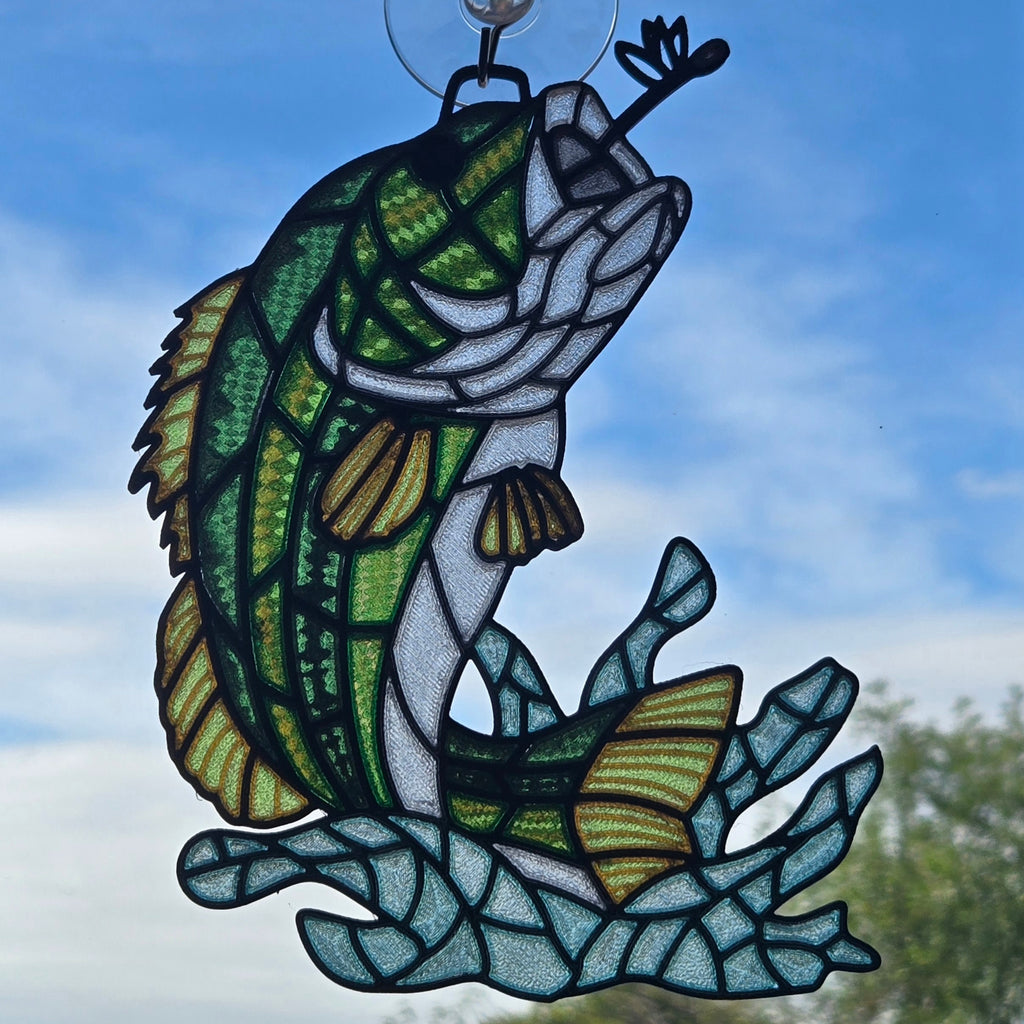 A 3d printed suncatcher depicting a jumping bass fish over blue water, suspended by a clear hook against a blue sky background.