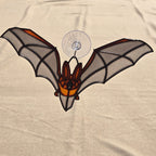 A 3D printed bat ornament with translucent gray wings, black outlines, and orange accents, attached to a clear suction cup against a beige fabric background.