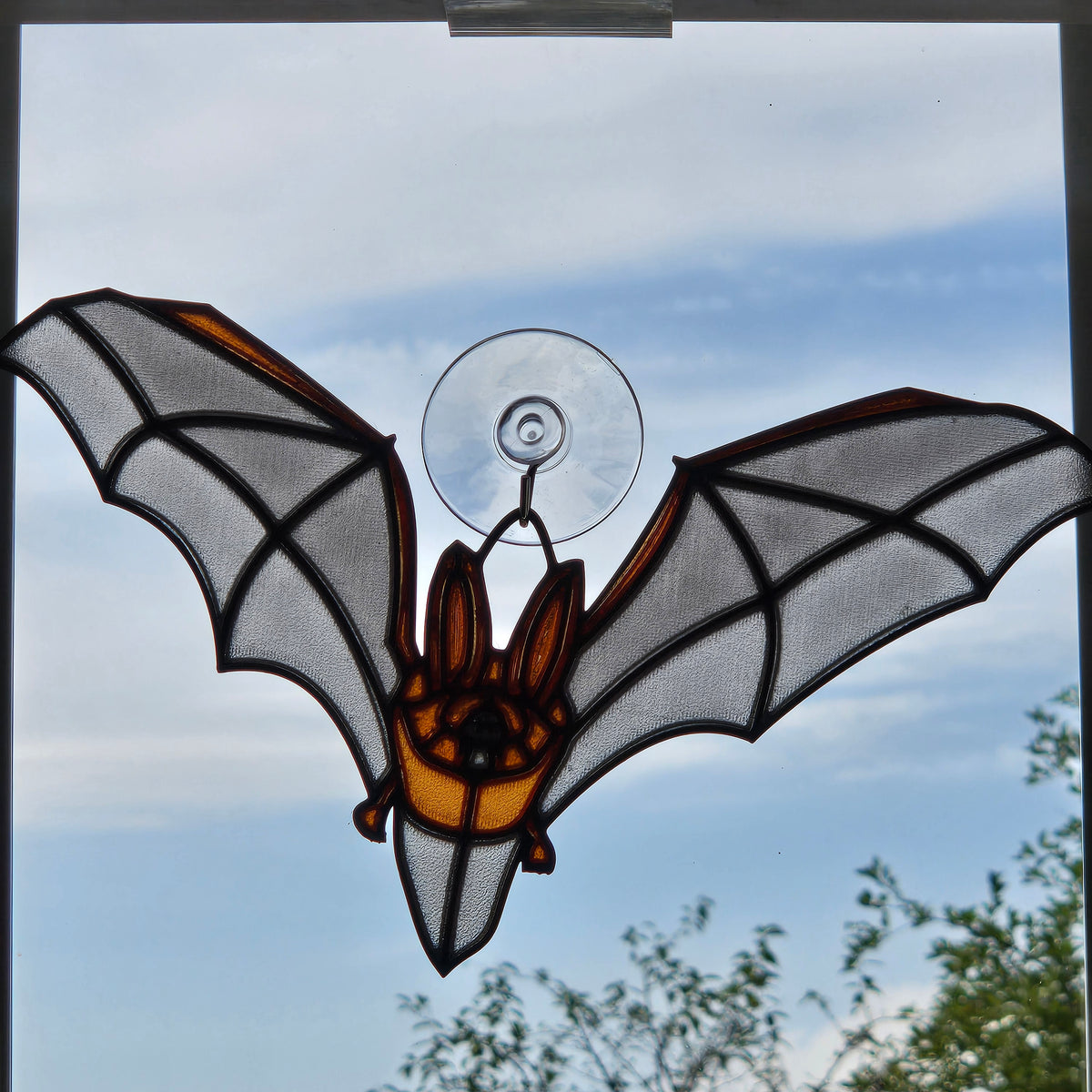 A bat-shaped 3D printed window hanging ornament with spread wings, attached to a clear suction cup, shown against an outdoor sky background.