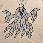 A ghost-shaped 3D printed ornament with a clear suction cup at the top, featuring a white and gray patterned body outlined in black, set against a beige fabric background.