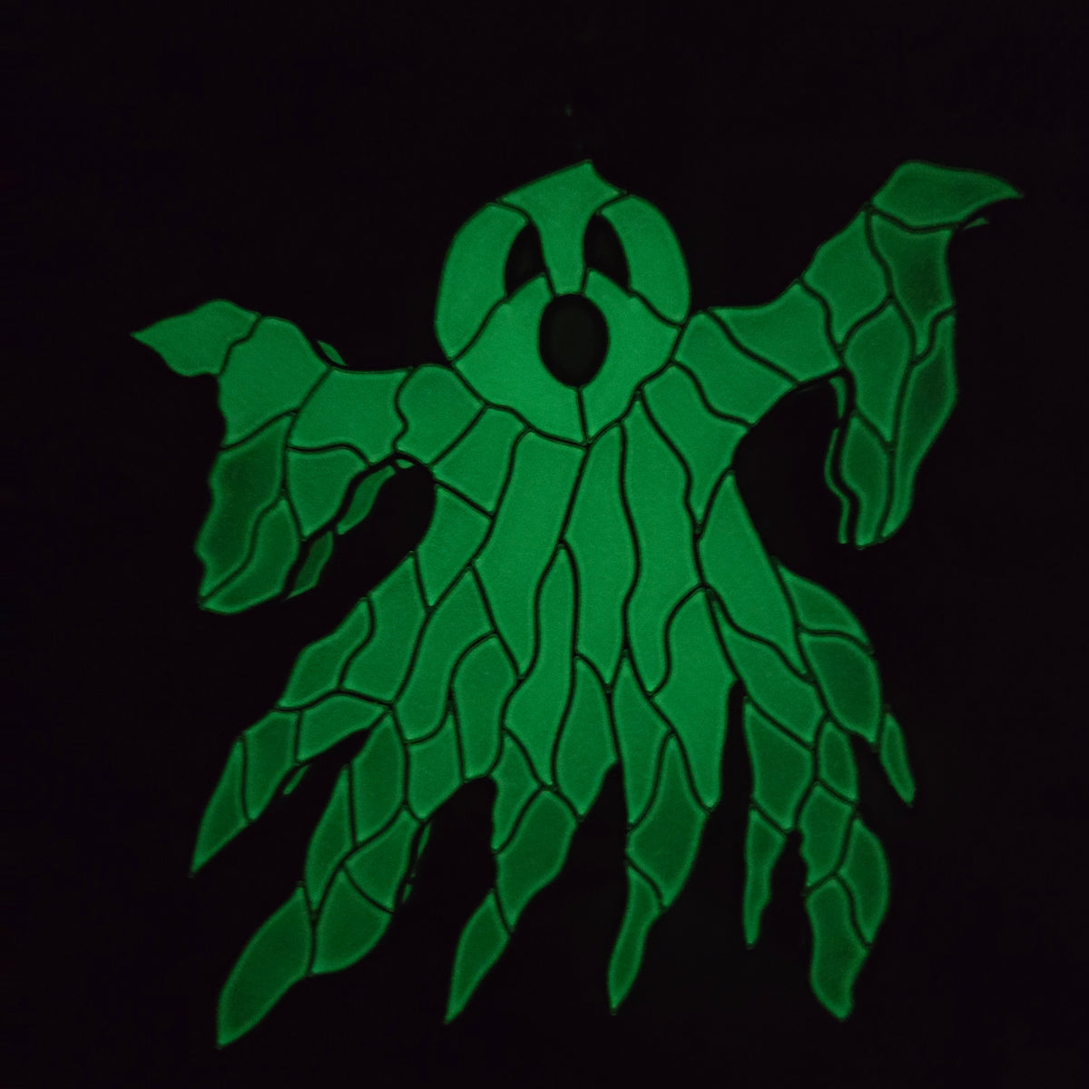 A green, leaf-like ghost suncatcher with a circular head and multiple leafy arms, shown on a black background.