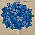 A 3D printed flower ornament depicting blue hydrangeas with green leaves, hanging from a clear loop at the top, set against a neutral beige background.