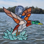 A 3d printed duck ornament with spread wings and a suction-cup mount, shown against a real outdoor water scene with trees in the background.