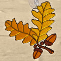 A 3D printed ornament depicting an oak branch with two large golden-yellow leaves and three brown acorns, outlined in dark metal and suspended from a clear suction cup.