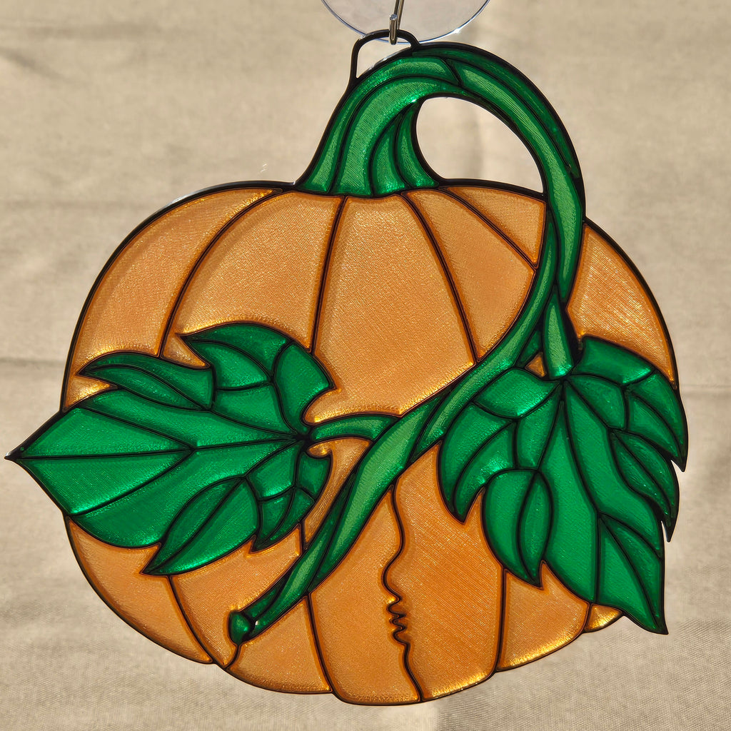 A 3D printed pumpkin ornament featuring a carved pumpkin design in orange with green stem, leaves, and vines. A small silver hanging loop is visible at the top against a neutral beige background.