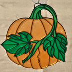 A 3D printed pumpkin ornament featuring a carved pumpkin design in orange with green stem, leaves, and vines. A small silver hanging loop is visible at the top against a neutral beige background.