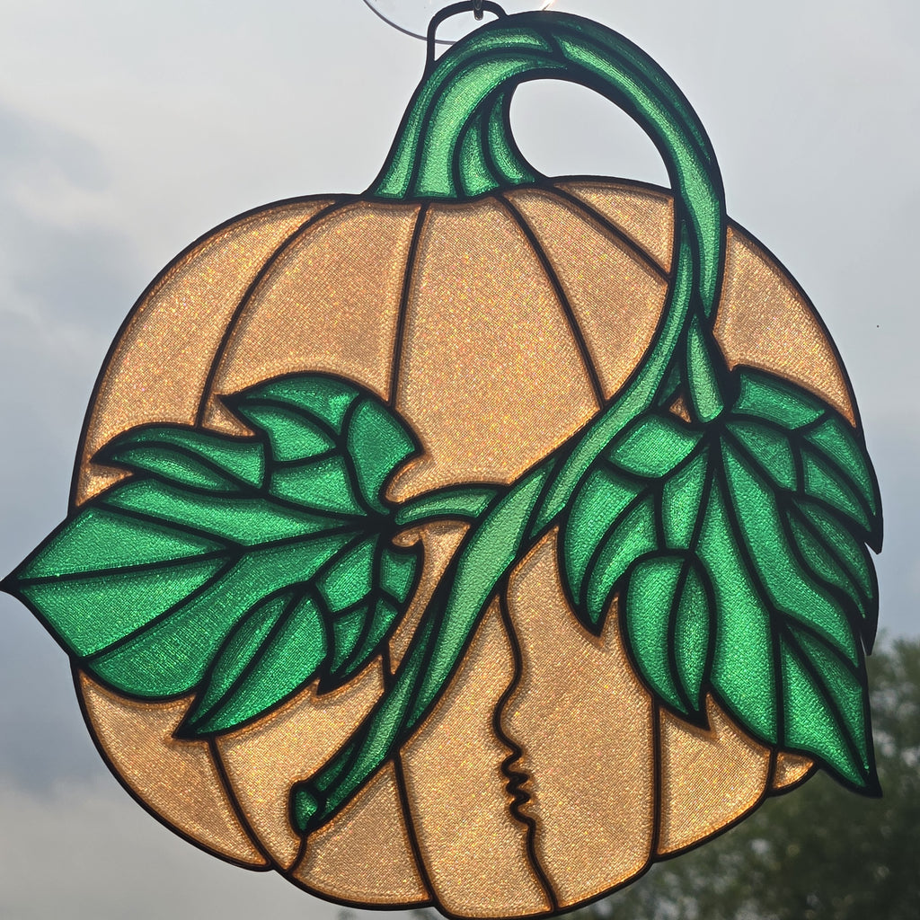 A 3D printed pumpkin ornament featuring a textured gold pumpkin body with a green stem, leaves, and a kissing couple's profile in the center, shown against an outdoor sky background.
