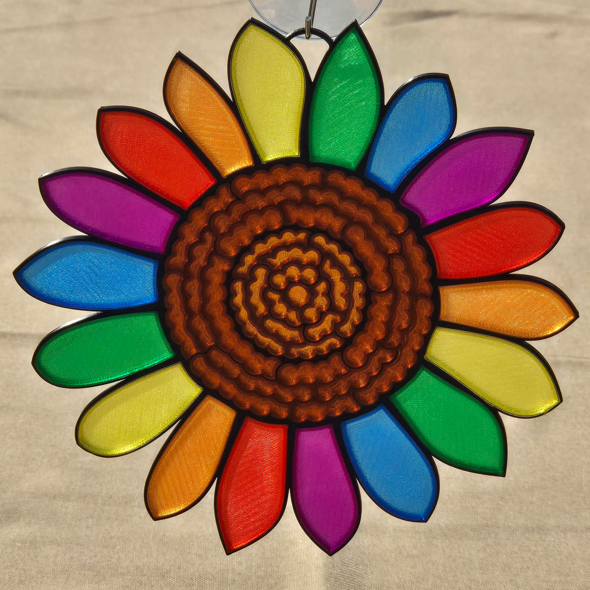 A 3D printed sunflower ornament with a brown textured center and rainbow-colored petals, hanging against a neutral beige background.