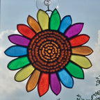 A 3D printed sunflower hanging in the sky, featuring a brown textured center and rainbow-colored petals outlined in black.