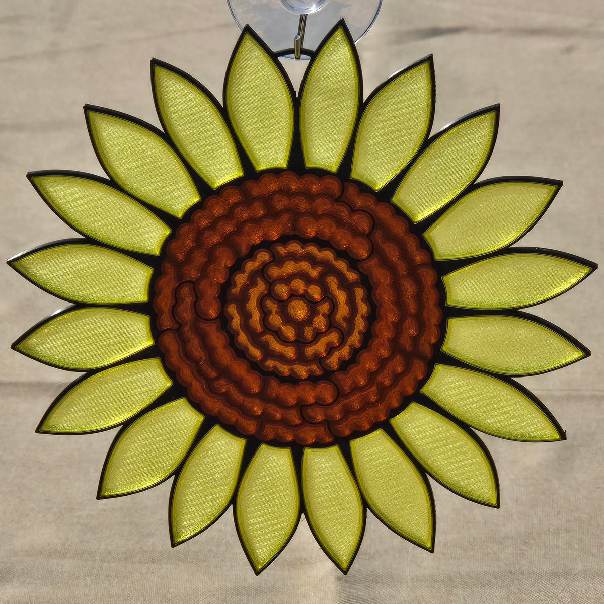 A 3D printed sunflower ornament with a textured brown center and bright yellow-green petals outlined in black, suspended by a clear hook at the top against a neutral background.