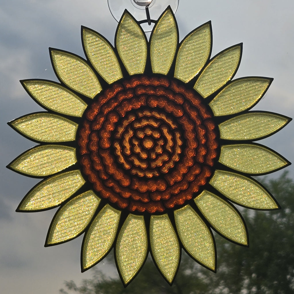 A 3D printed sunflower ornament hanging against an outdoor sky background, featuring textured pale yellow petals and a detailed brown glass center.